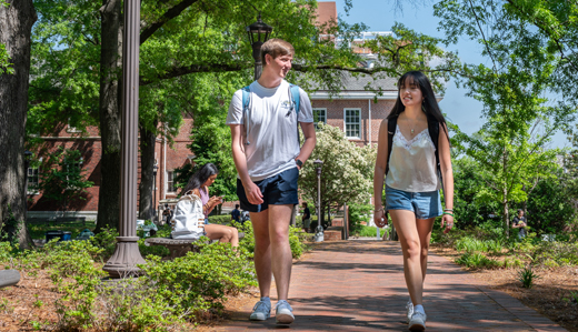 Two Georgia Tech undergraduate students walk down a campus sidewalk near Harrison Square on campus in Atlanta, Georgia.